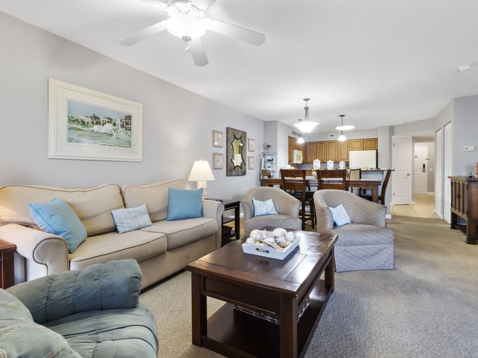 Relax in your spacious living room featuring plush seating, coastal artwork, and an open layout connecting to the dining area and kitchen.