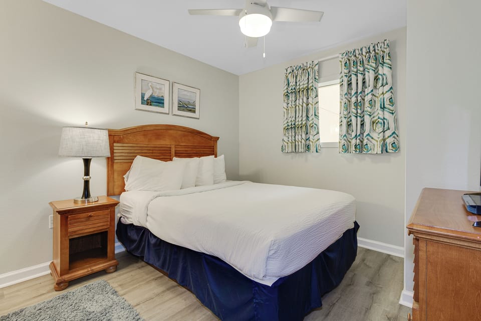 Rest peacefully in your comfortable bedroom with crisp linens, warm wood furnishings, and gentle natural light filtering through coastal-themed curtains.