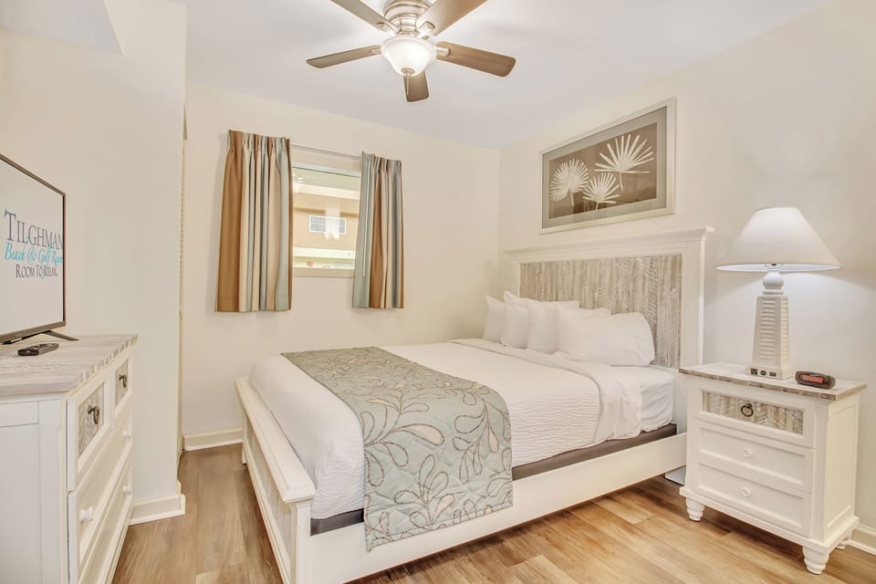 Unwind in your serene coastal-themed bedroom with a plush bed, gentle ceiling fan, and warm wooden floors for ultimate relaxation.