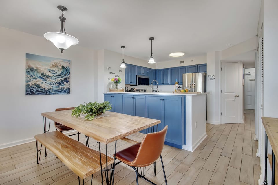 Your open-concept space flows beautifully from dining to kitchen, where ocean-inspired blue cabinets create a coastal vibe perfect for vacation cooking.