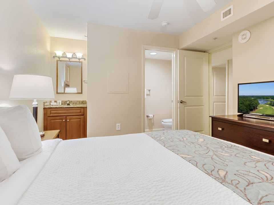 Unwind in your spacious bedroom featuring a plush king bed, vanity area, and private bathroom—all with peaceful lake views.