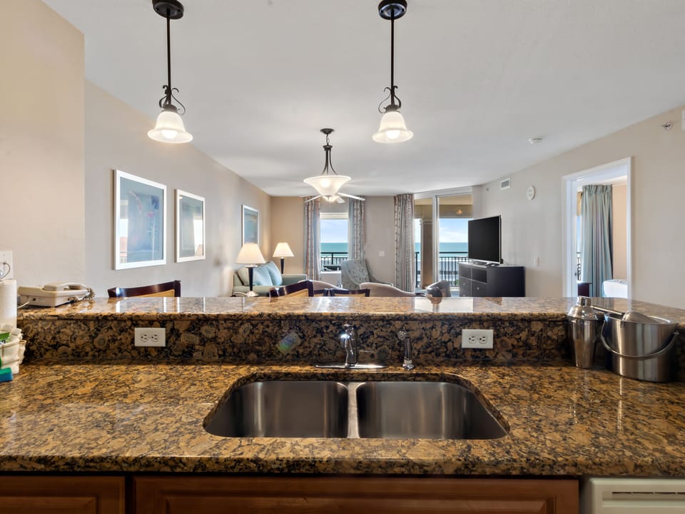 Cook with ocean views from your granite kitchen island, where elegant pendant lighting illuminates meal prep while waves sparkle beyond your balcony.