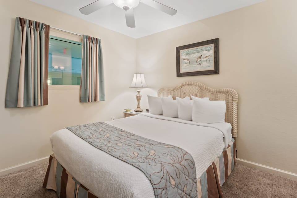 Drift off peacefully in your cozy bedroom featuring crisp linens, gentle coastal artwork, and a ceiling fan for comfortable nights.