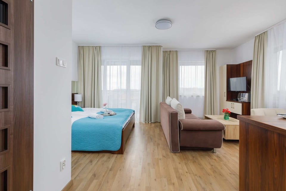 A bedroom with bedside lamps, neatly arranged blue bedding, and large windows.