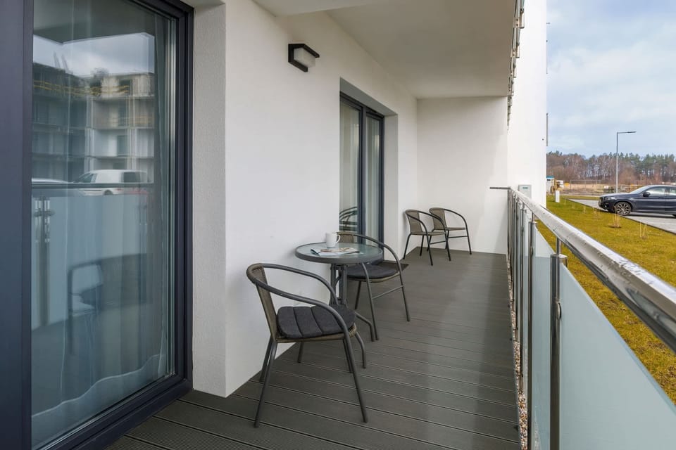 A balcony area with a small table and chairs, ideal for enjoying outdoor relaxation. The view overlooks the apartment complex and its surroundings.