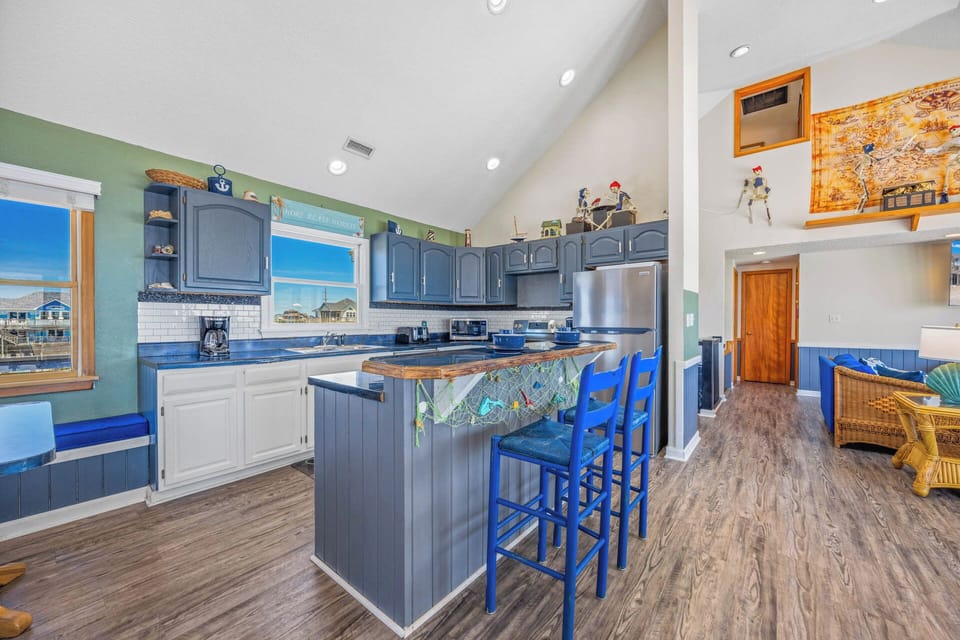 Step into your bright, open kitchen with coastal charm, where ocean views through the windows meet playful blue accents. The island invites you to gather over morning coffee while soaking in the light and relaxed vibe.