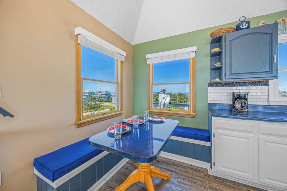 Bright coastal kitchen with cheerful blue accents, built-in seating, and windows framing neighborhood views—perfect for morning coffee or meal prep during your stay.
