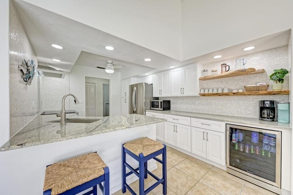 The kitchen includes full sized appliances, a beverage fridge, shell tile backsplash, and custom Norfolk Island Pine floating shelves.