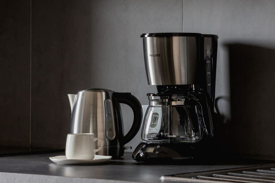 A small coffee setup featuring a black coffee machine, a kettle, and cups. The wooden countertop adds warmth to the space.