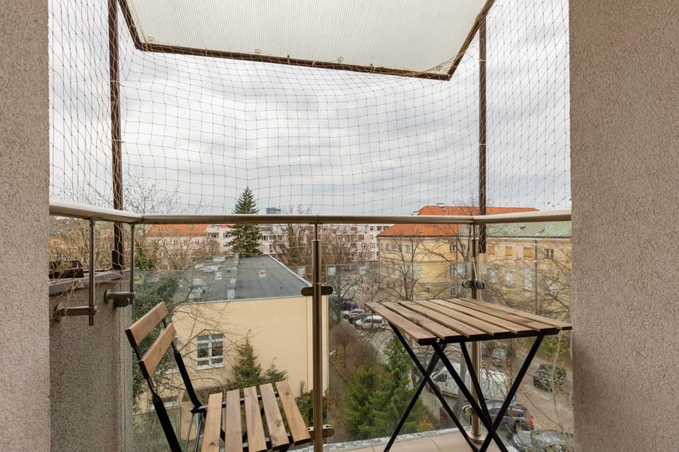 A small balcony featuring a table and chairs, overlooking a scenic urban landscape.