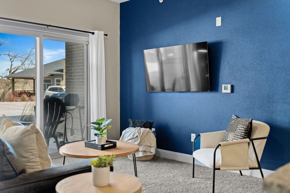 Bright living space anchored by a bold accent wall, wall-mounted TV, and comfortable seating. Natural light pours in through the sliding doors, creating an easy spot to unwind, stream your favorites, or step outside to the patio.