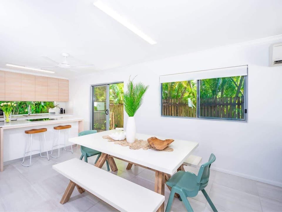 Gather around the dining table for shared meals while tropical greenery frames every window and fills the space with natural light.