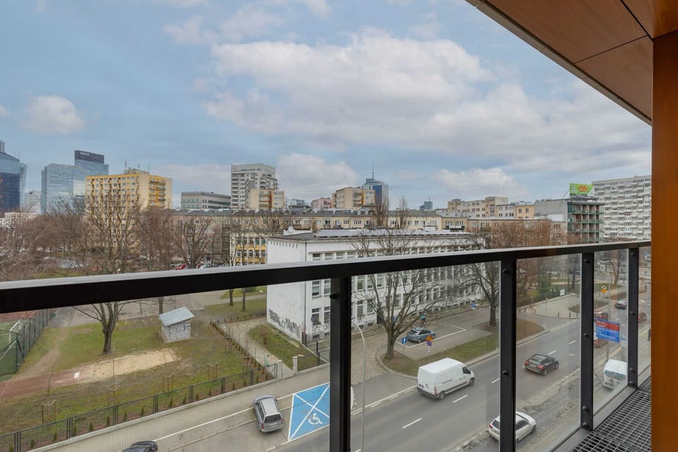 A modern balcony overlooking a cityscape. The railing is made of glass, providing an open and unobstructed view.