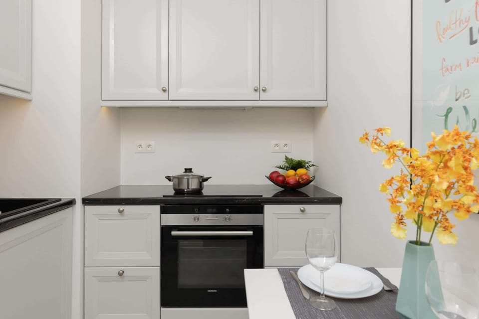 A compact kitchenette with white cabinetry and black countertops. A vase with fresh flowers adds a cheerful touch.