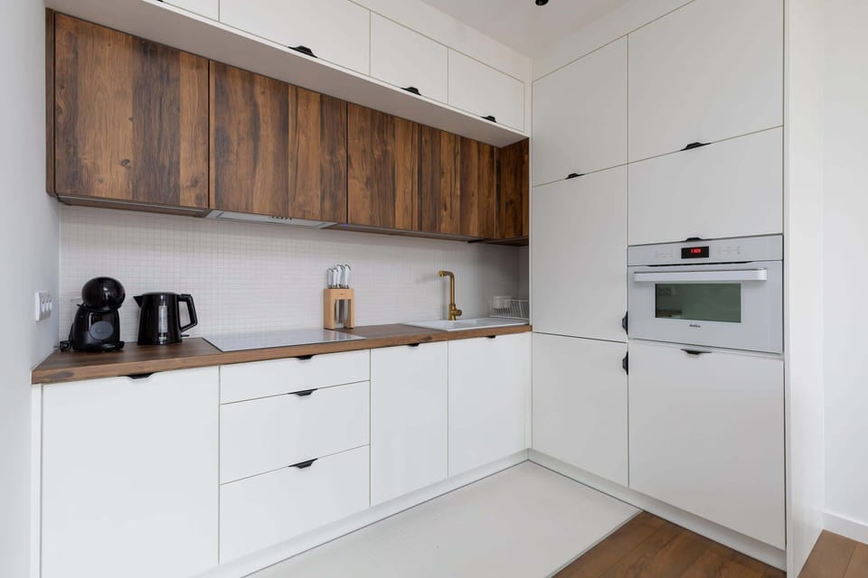 A modern kitchenette featuring white cabinets and wooden upper shelves, complemented by a black countertop.