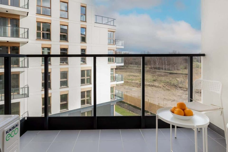 A modern balcony with a small table and chairs, perfect for enjoying fresh air. The view overlooks a serene garden area.