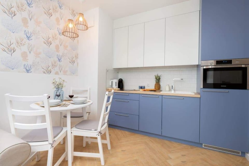 A light blue and white kitchen with modern appliances and a dining table with chairs.

