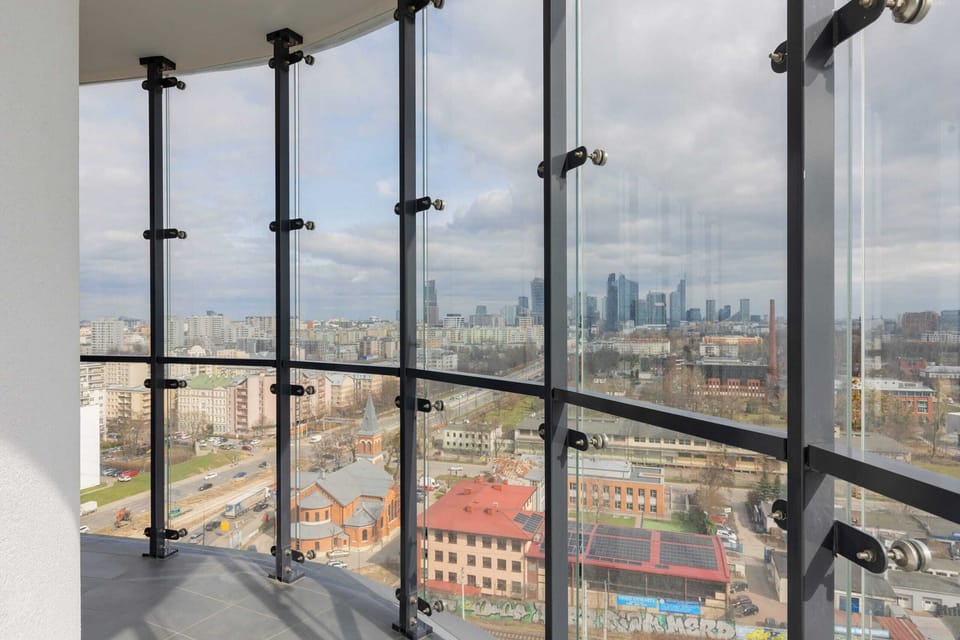 A panoramic view from the apartment showcasing an urban skyline under a cloudy sky. The expansive windows enhance the feeling of openness.