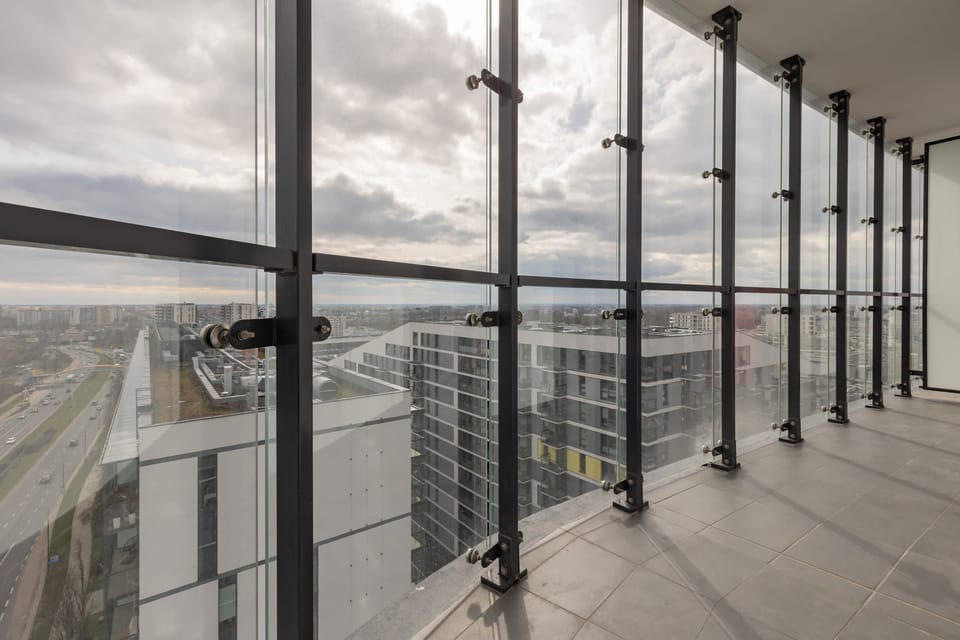 A spacious balcony with transparent glass panels and sweeping views of the city. The area is perfect for relaxation or enjoying morning coffee.