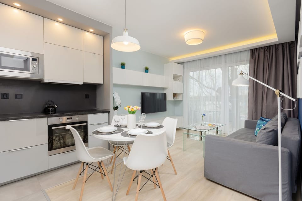 A modern kitchen with white cabinetry, an adjacent dining table, and hanging lights.