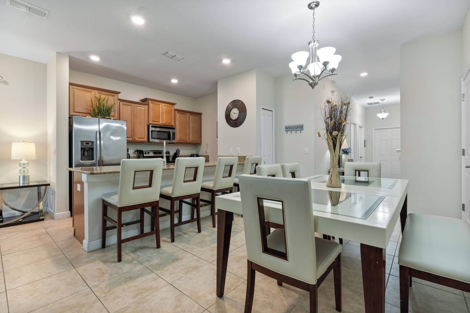Enjoy meals in this bright dining area with a sleek glass table and comfy cream chairs, all set against warm wood cabinetry and stainless-steel appliances in the modern kitchen, highlighted by stylish pendant lighting above.