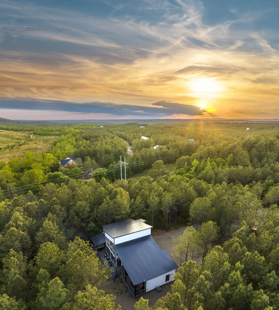 Modern cabin nestled in the forest of Hochatown, illuminated by sunset hues. 