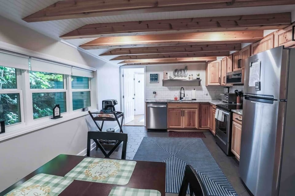 Discover culinary delight in our expansive, fully stocked kitchen, where stainless steel appliances, granite countertops and a subway-style backsplash harmonize seamlessly beneath the rustic charm of exposed beams and sleek grey tile flooring 