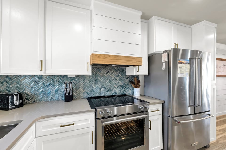 Your gourmet kitchen features sleek white cabinetry, stunning chevron tile backsplash, and premium stainless steel appliances for memorable meal prep.