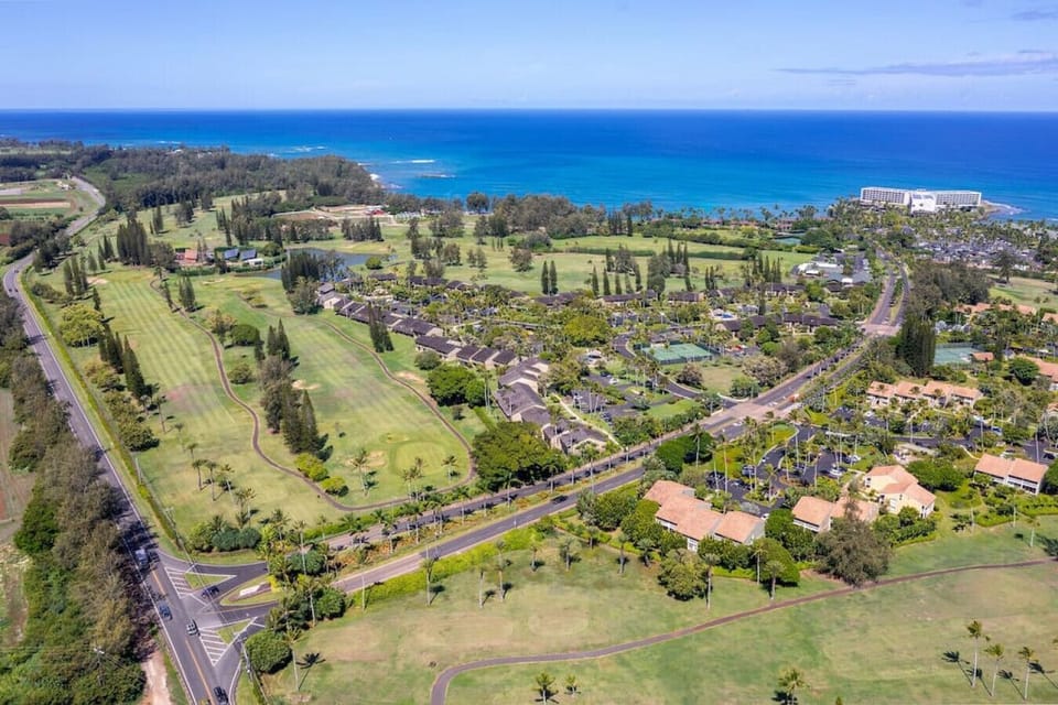 Aerial view capturing rolling hills, open greens & coastal charm.