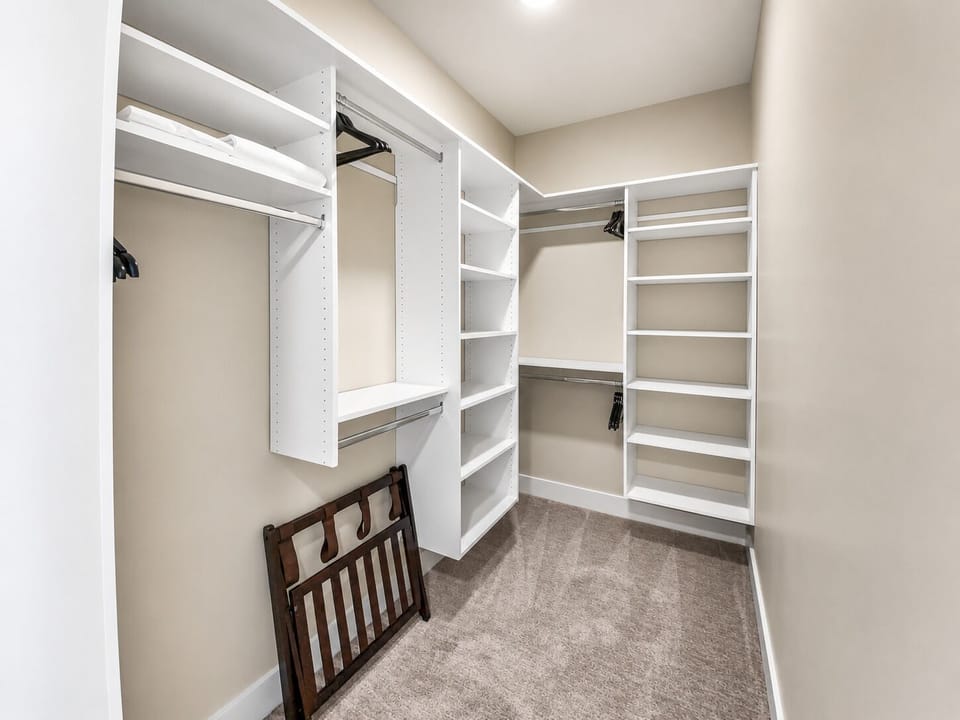 This spacious walk-in closet features custom white shelving with adjustable racks and hanging rods, providing ample storage for your wardrobe and belongings throughout your stay.