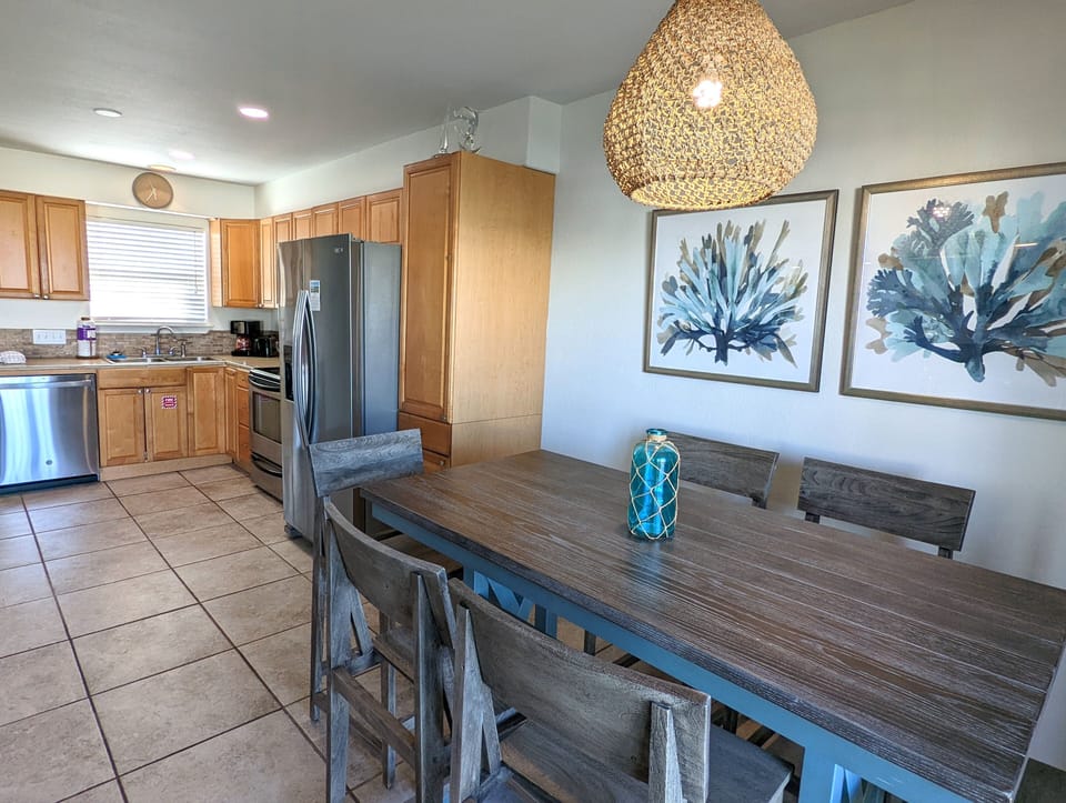 Gather around your spacious dining table for memorable meals, with a fully-equipped kitchen featuring modern appliances and coastal-inspired decor creating the perfect home base.
