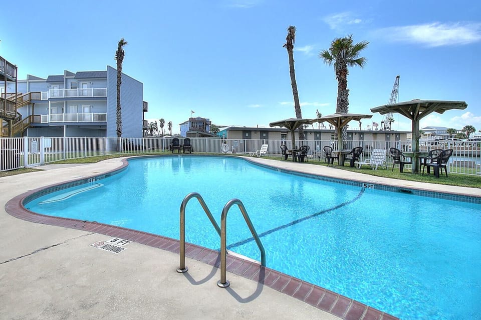 Crystal-clear pool with shade structures and seating areas creates your perfect poolside retreat under sunny skies.