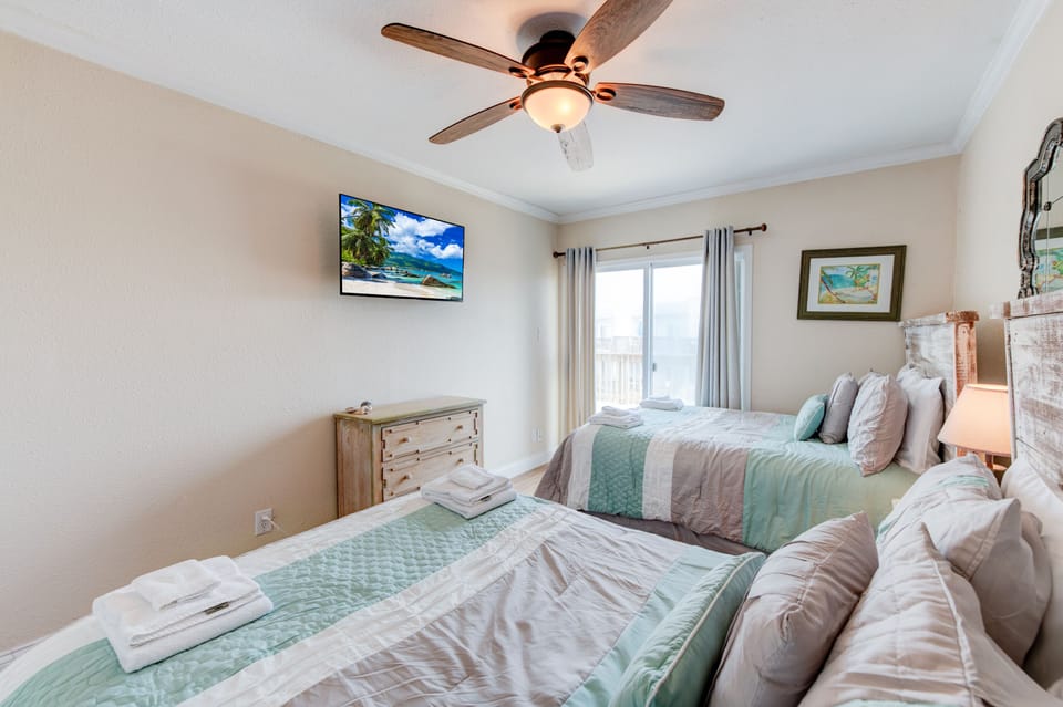 Drift into peaceful sleep in your serene twin bedroom, complete with ceiling fan, beach-themed TV, and soft coastal linens.