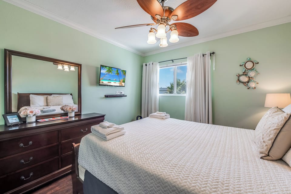 Relax in your soothing bedroom with soft mint walls, ceiling fan, wall-mounted TV, and tropical views from your window.