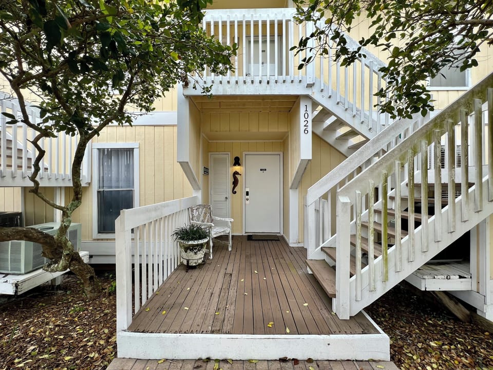Charming coastal cottage entrance with peaceful deck space where you can unwind under mature trees.