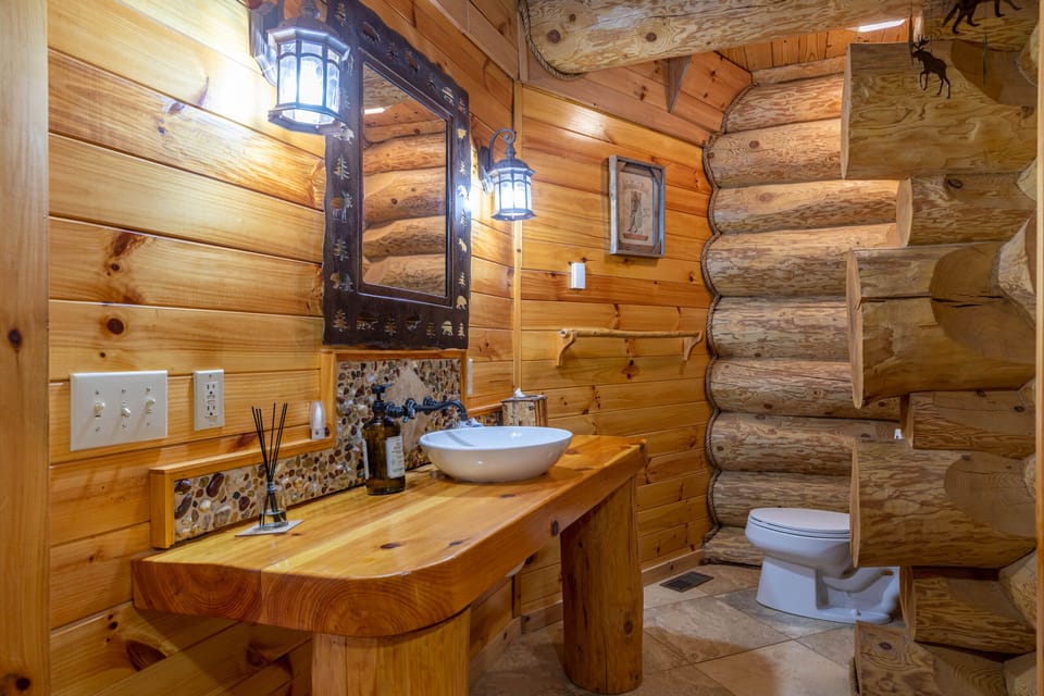 Rustic charm meets craftsmanship in this log-walled bath, featuring a live-edge vanity and hand-carved mirror frame.