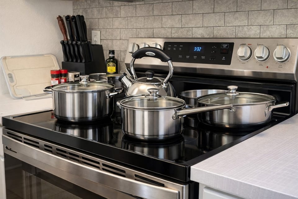 Fully equipped kitchen with stainless steel pots and kettle on a modern electric stove with a tiled backsplash.
