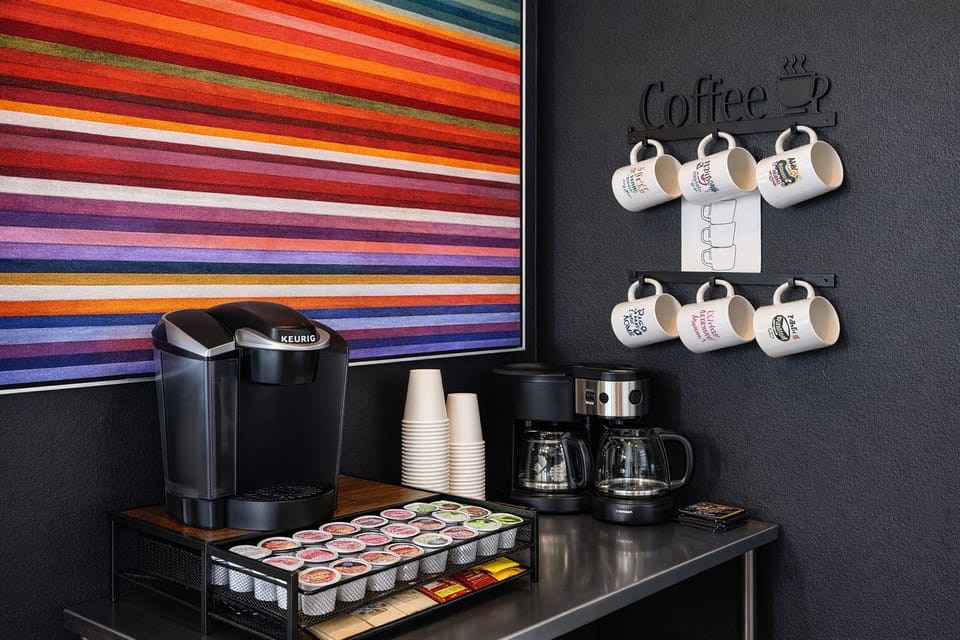 Fully stocked coffee station with multiple brewing options and a colorful striped wall art