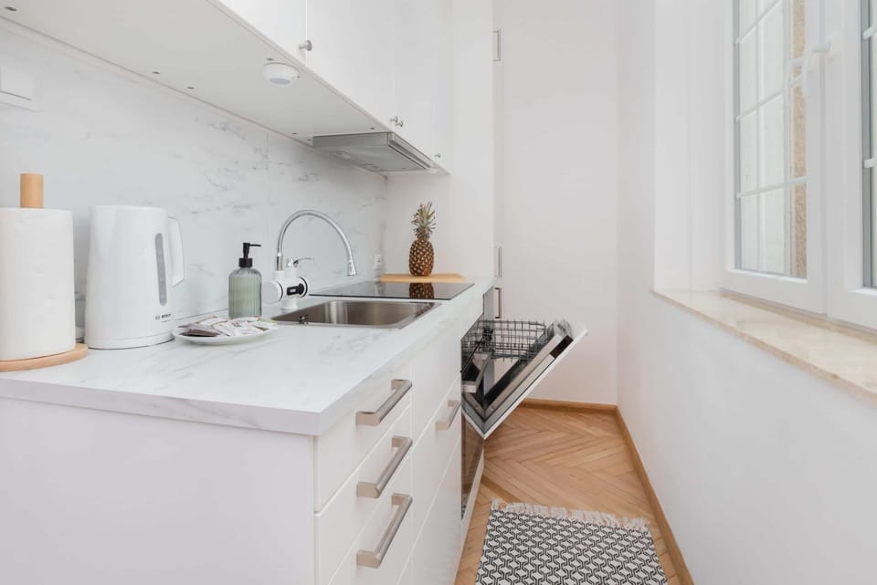 A bright and modern kitchen area with a marble countertop, sink, and white appliances for a clean look.
