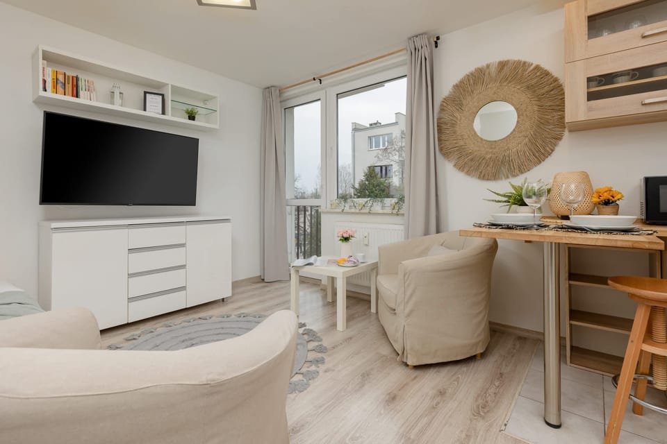 A modern setup with a sleek white dresser, a flat-screen TV, and a cozy armchair, accented by neutral tones and minimalist decor.