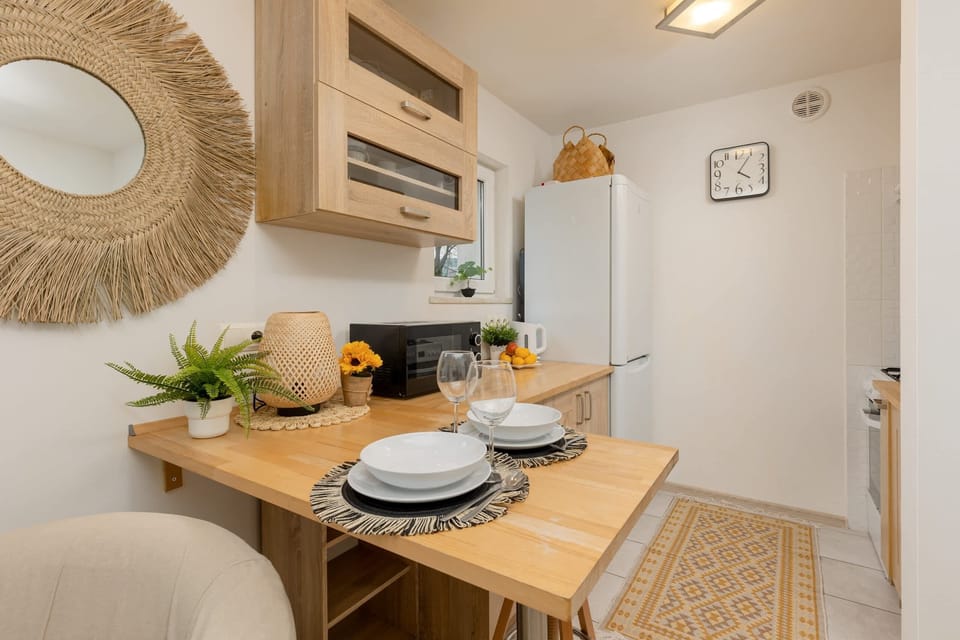 A bright and welcoming corner with wooden furniture, a small dining table, and a large window bringing in natural light.