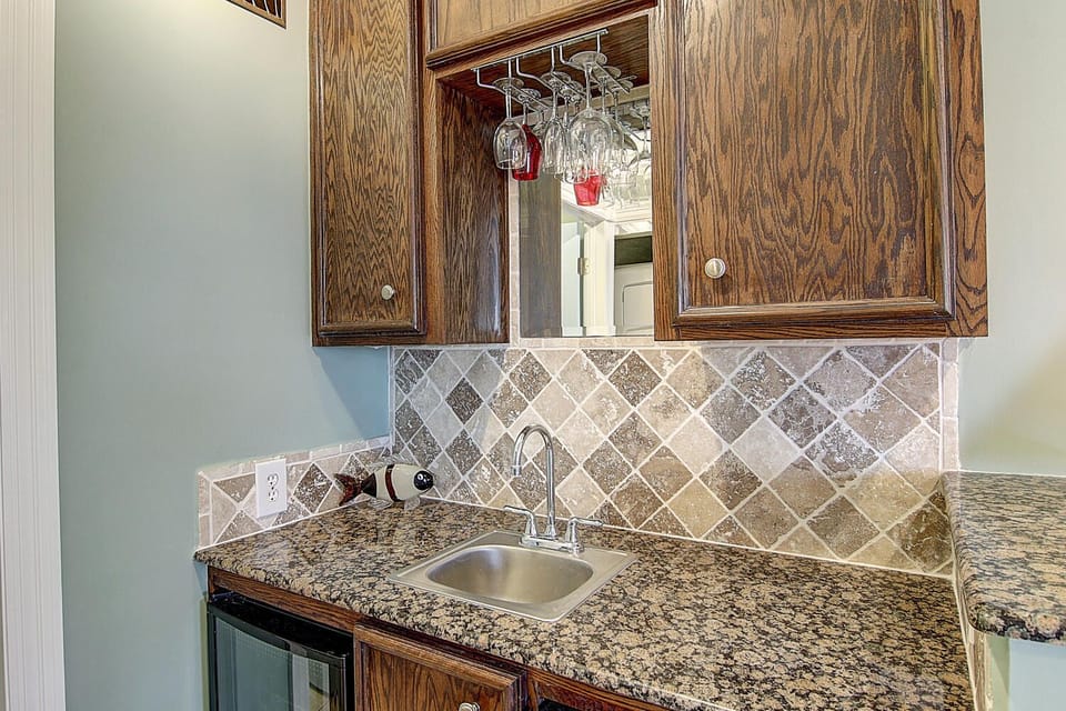 Your elegant kitchenette features rich wood cabinetry, granite countertops, and a stunning diamond-pattern backsplash perfect for preparing light meals.