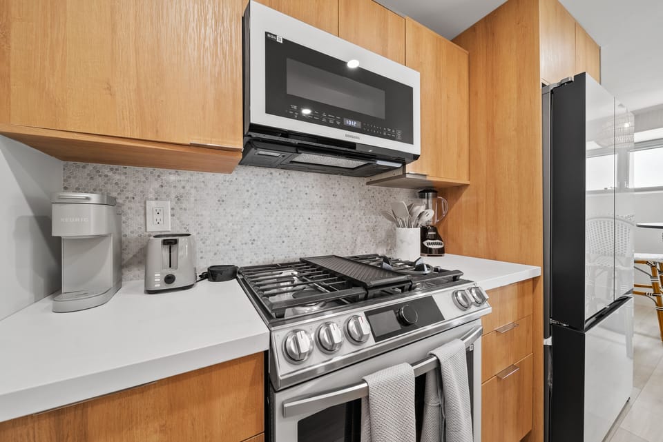 Kitchen with microwave, stove, coffee maker, and refrigerator - Prepare island-inspired meals in a thoughtfully updated kitchen featuring a gas stove, full-size refrigerator, and warm wood cabinetry—perfect for extended stays in Waikiki.