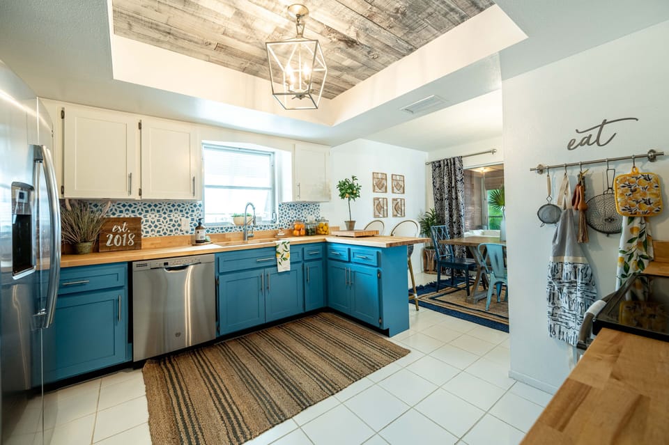 Kitchen with two-tone cabinets, butcher block countertop, pendant lights, stainless dishwasher, and EAT sign