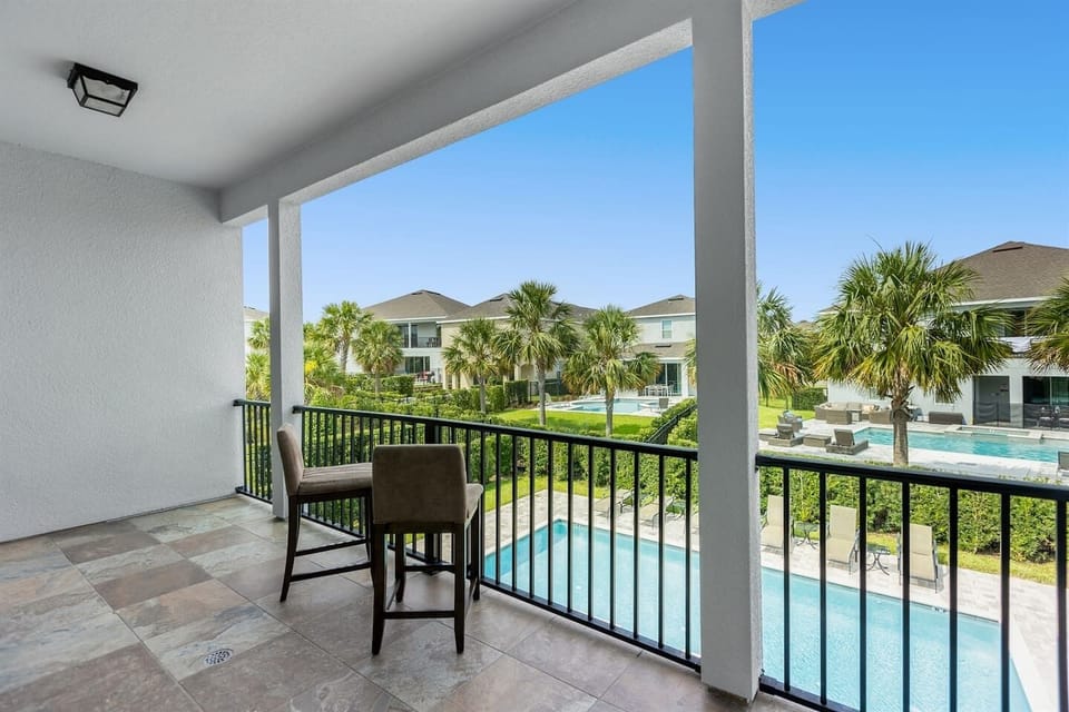 The patio features two stylish chairs with soft cushions, positioned to overlook a sparkling blue pool.