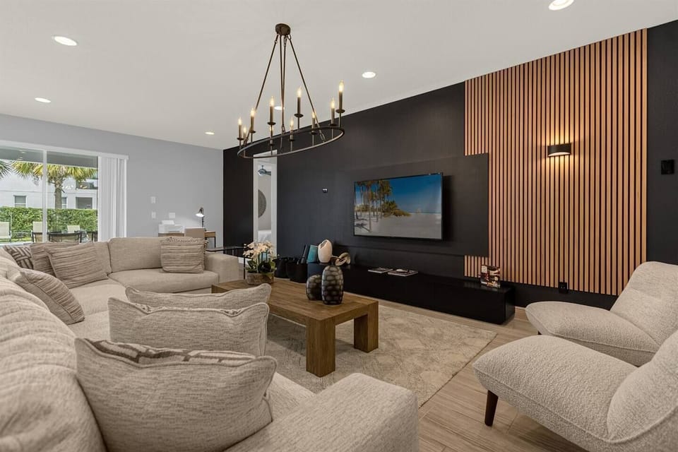 A spacious living room with a chic, stylish sofa adorned with plush cushions. A sleek smart TV is mounted on the wall, surrounded by an aesthetic design of modern accents and soft lighting, creating a cozy yet elegant vibe. Perfect for relaxation!