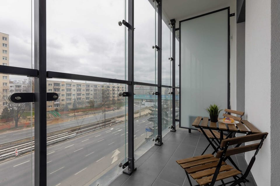 A modern balcony with seating, overlooking a vibrant urban environment with glass railings for an unobstructed view.