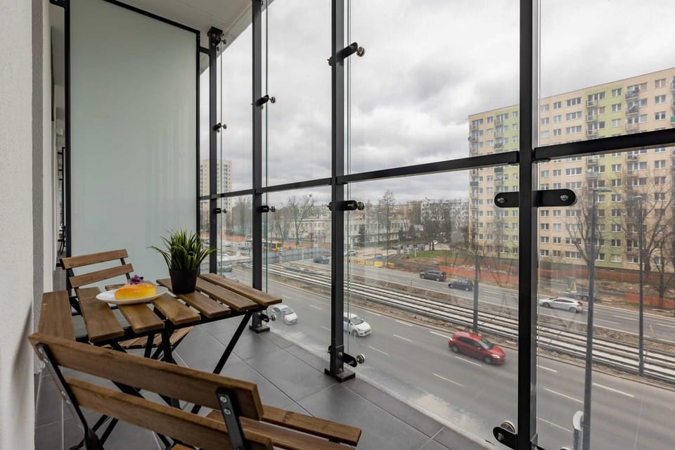 A modern balcony with seating, overlooking a vibrant urban environment with glass railings for an unobstructed view.