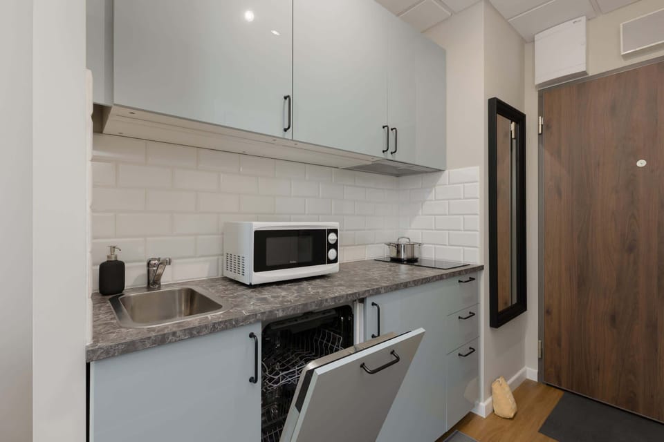 A compact kitchen with light cabinets, a microwave, and a tiled backsplash for a clean, modern look.