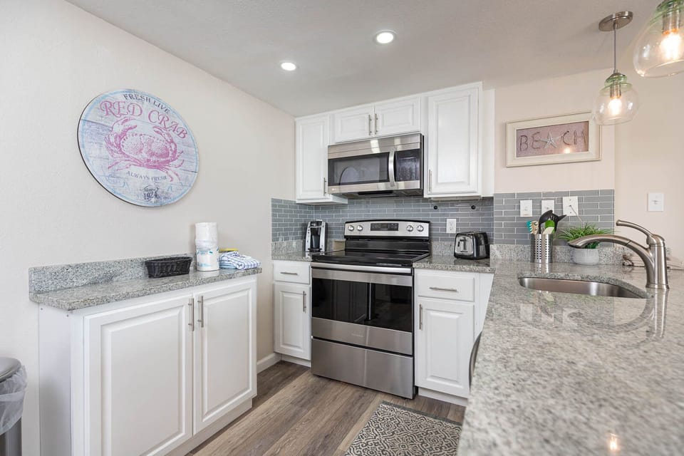 The kitchen features sleek stainless appliances, granite countertops, and beach-themed decor, perfect for culinary adventures